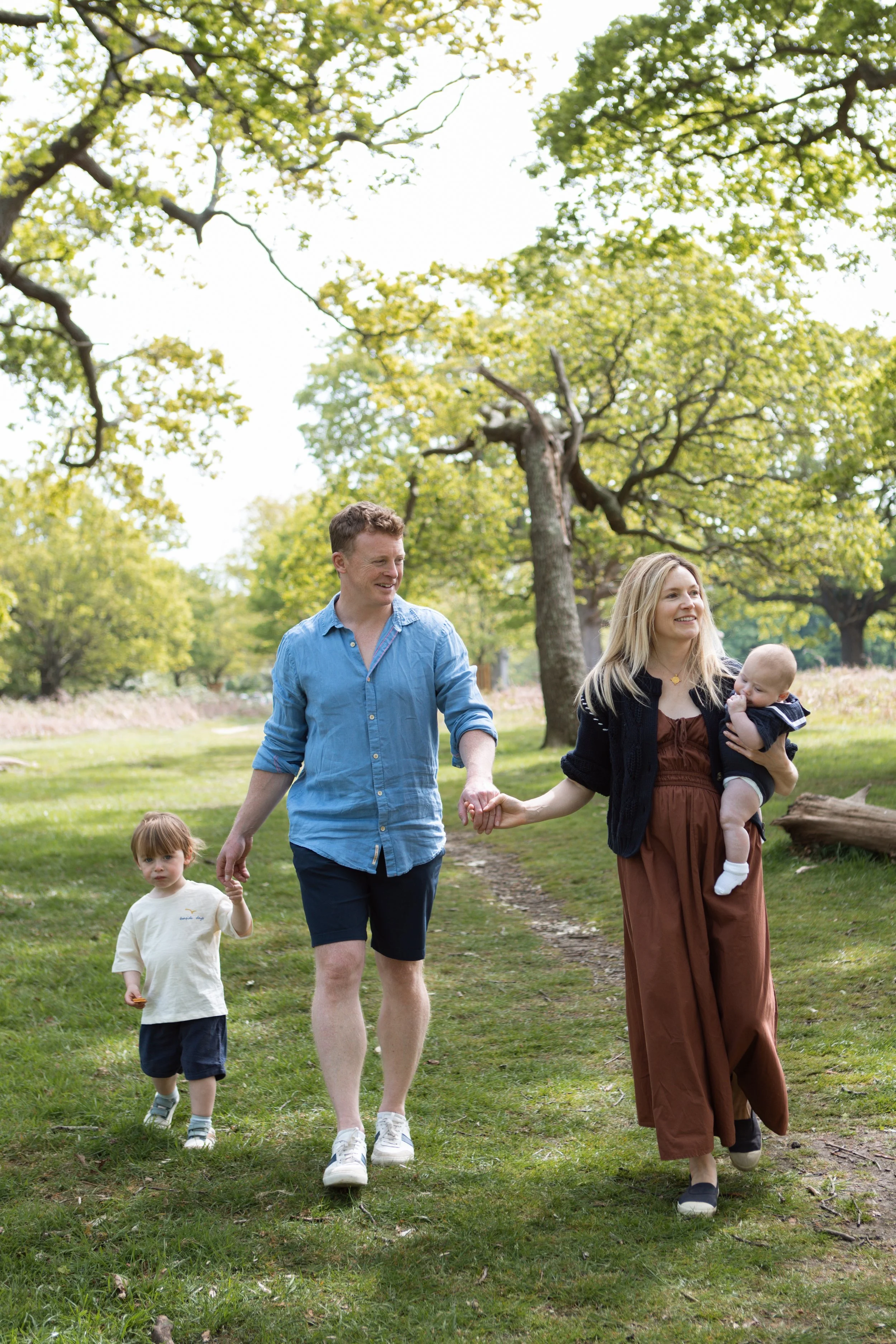 Family walking through a park on a sunny day, with trees and greenery around.