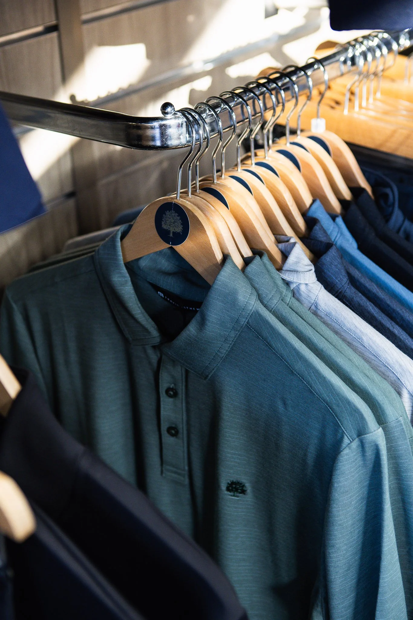 Men's dress shirts hanging on wooden hangers on a metal rod in a clothing store.