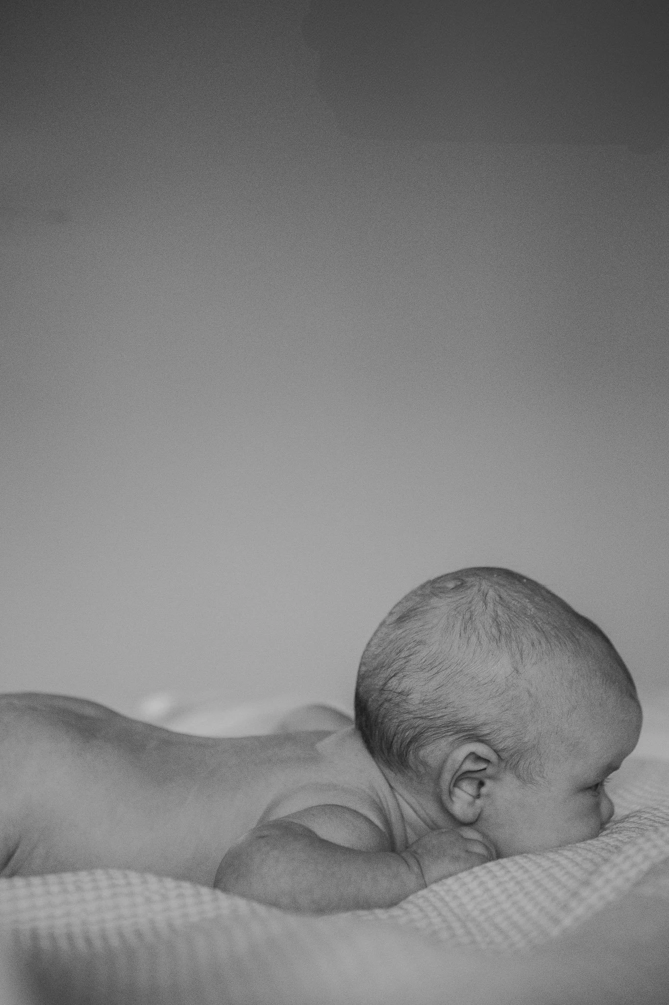 A sleeping baby with a bald head lying on its stomach on a soft surface.