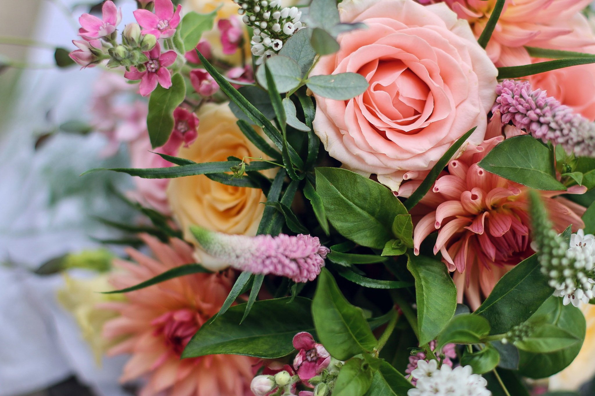 Close-up of a floral bouquet with pink roses, pink lilies, white and pink small flowers, and green leaves.