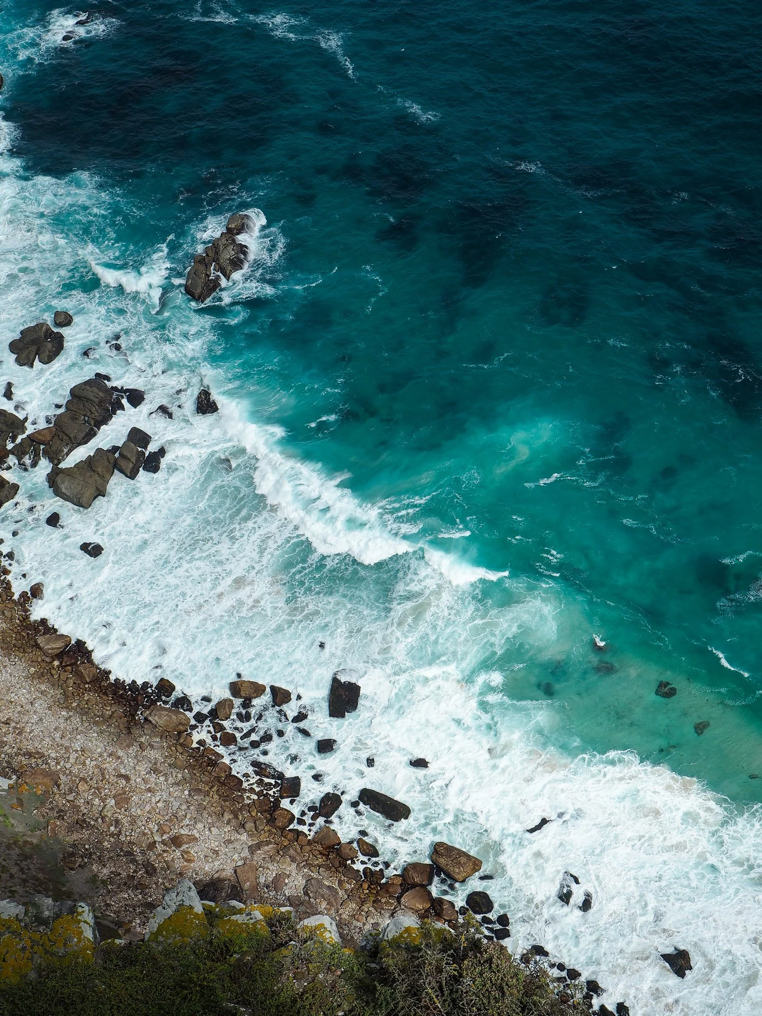 Aerial view of rocky coastline with waves crashing onto shore and deep blue ocean.