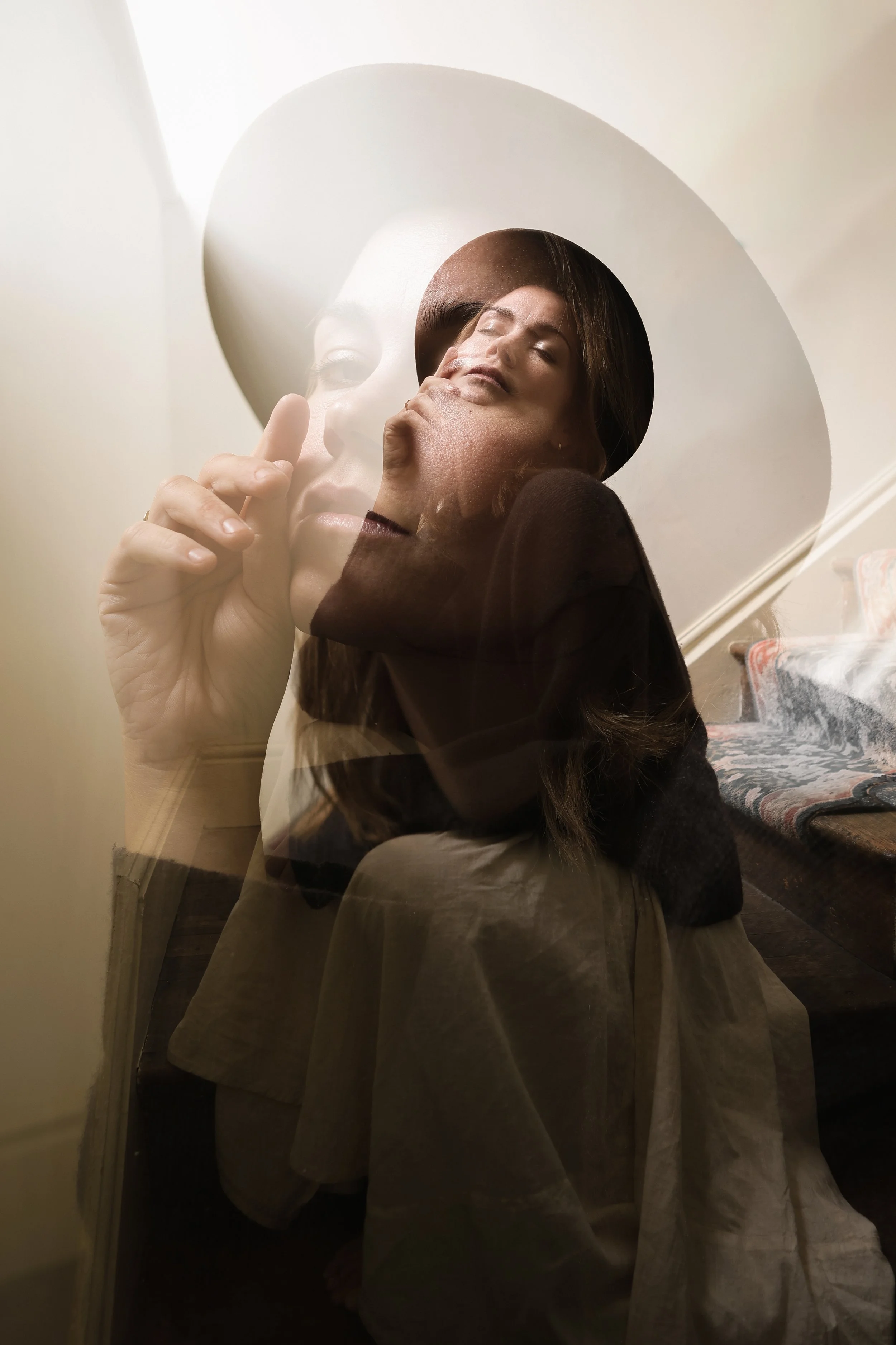 A woman looking in a mirror with a double exposure effect creating a layered appearance, wearing a wide-brimmed hat and a dark top.