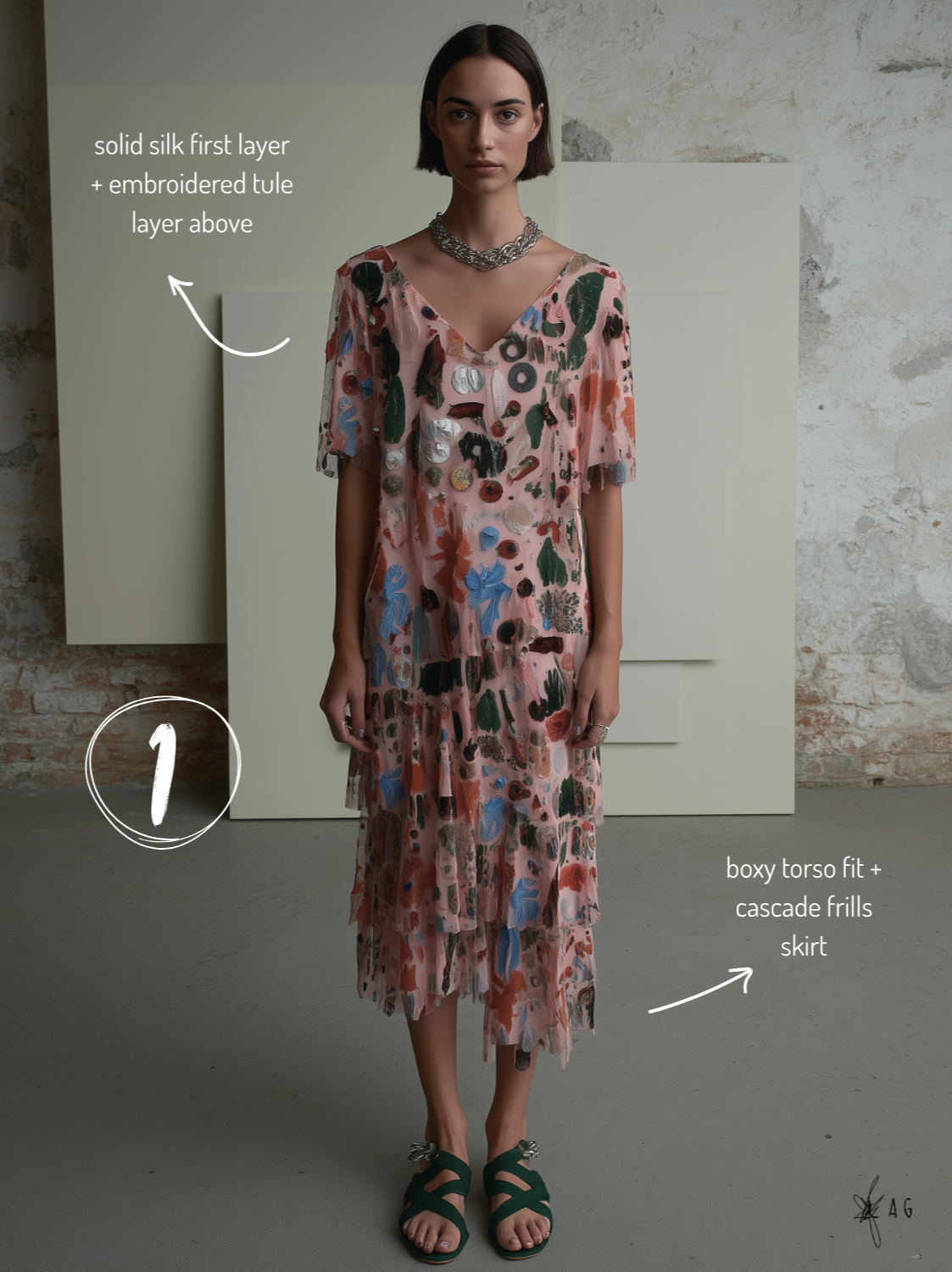 A woman wearing a layered, colorful, printed dress with a solid silk first layer and embroidered tile layer above. She is accessorized with a chunky silver necklace and sandals, standing in front of a textured wall with abstract geometric backgrounds