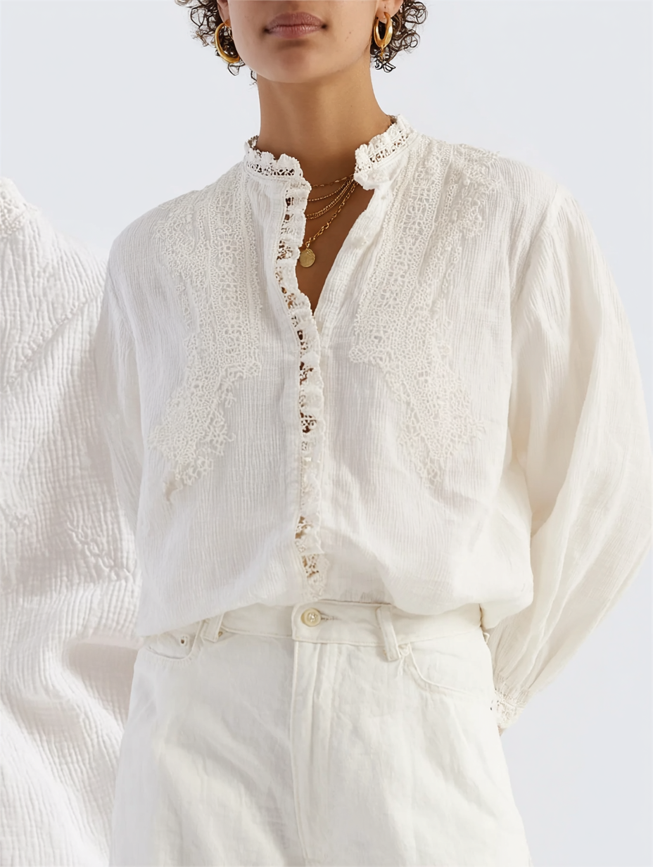 A woman wearing an elegant white blouse with lace and embroidery details, paired with white high-waisted pants, accessorized with gold hoop earrings and layered gold necklaces.