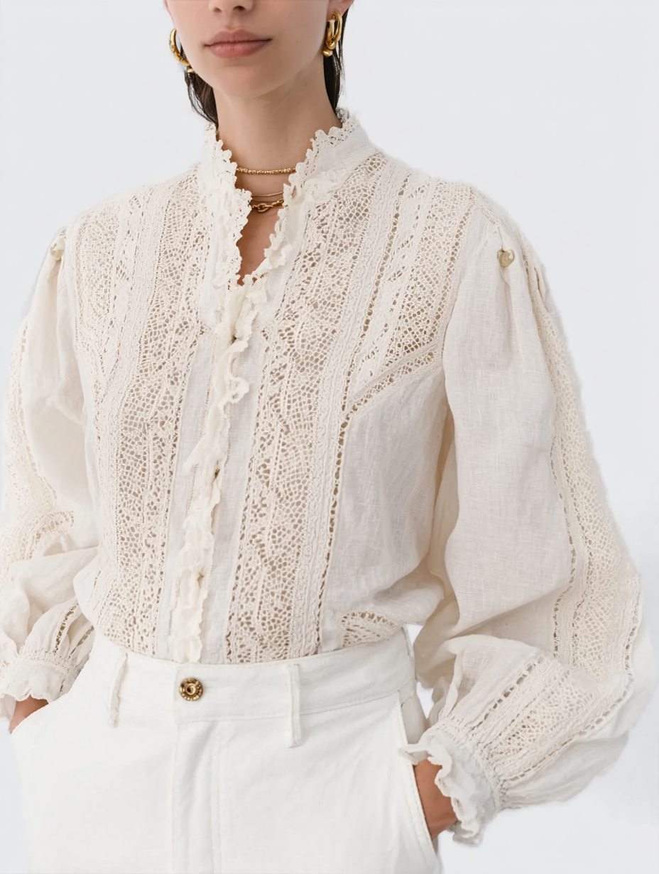 A woman wearing a white lace, embroidered blouse with ruffled details and high-waisted white pants, accessorized with gold jewelry.
