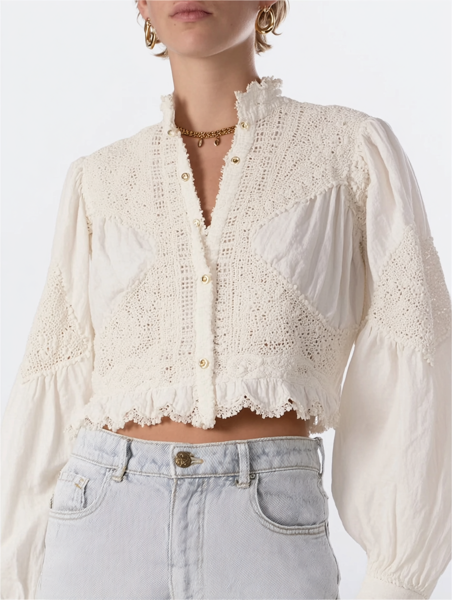 A person wearing a cream-colored, crocheted, long-sleeve crop top with lace details and pearl buttons, paired with light gray high-waisted jeans. The person has gold hoop earrings and a gold necklace.