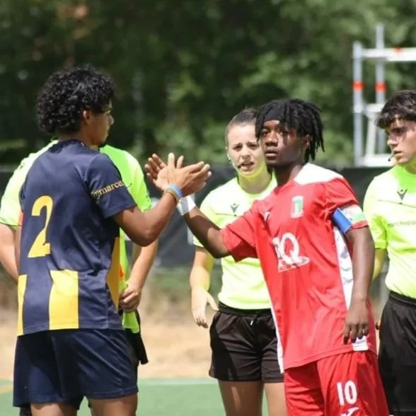 Jugadoras de fútbol de diferentes países en un campo, saludándose y dándose la mano antes del partido.