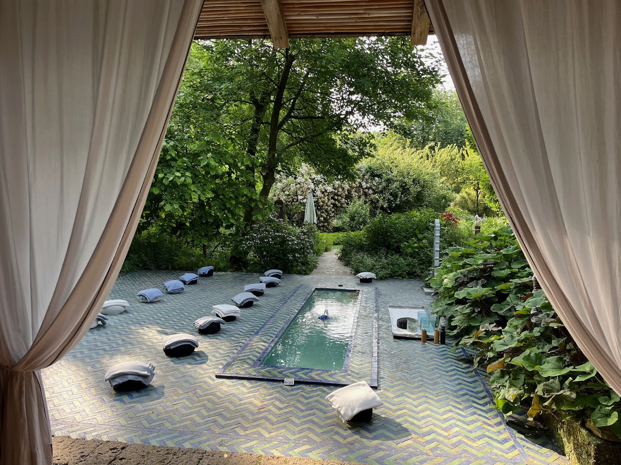 Buitenterras met zonnedak, tuin, een zwembad en stoelen met kussens.