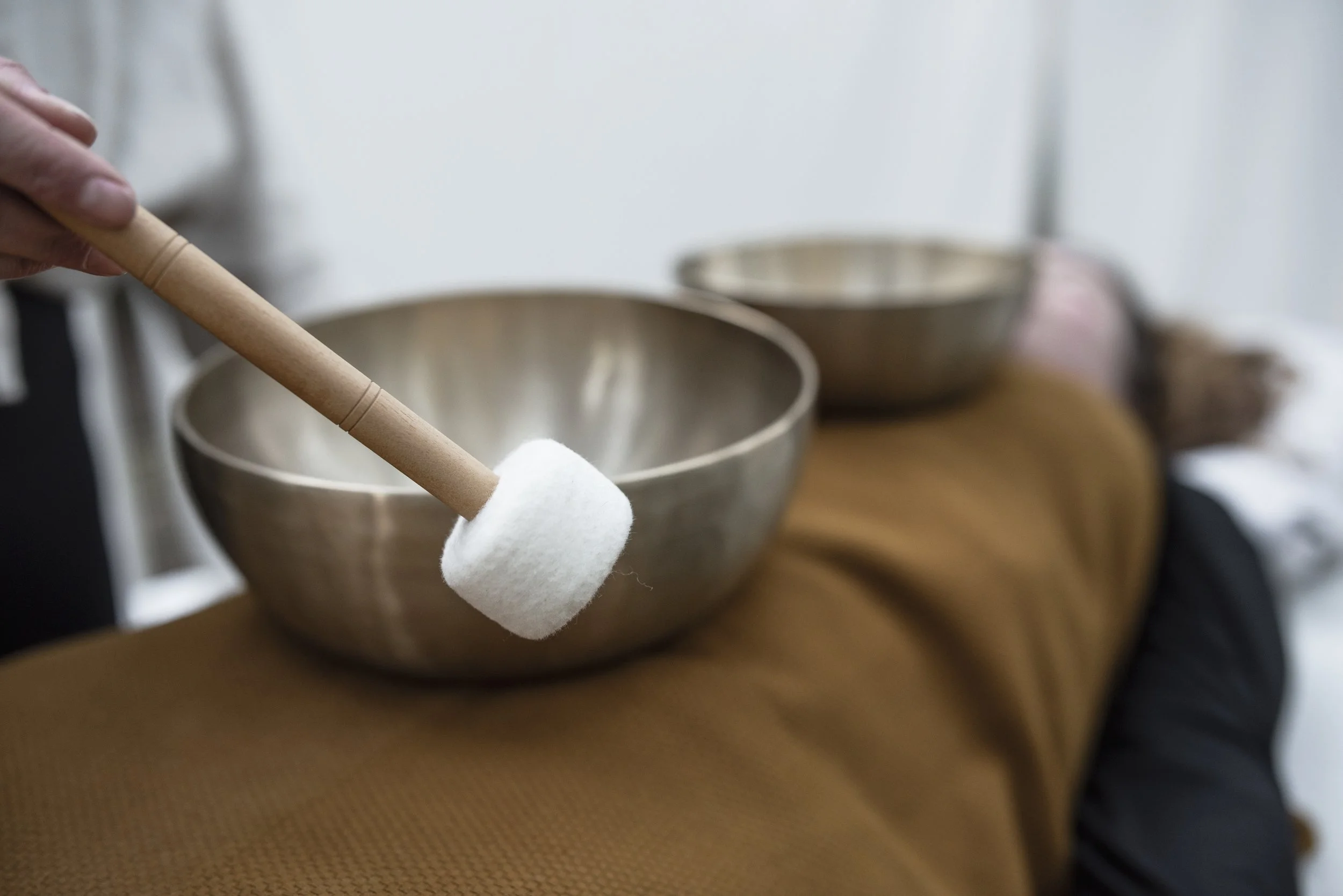 A person resting with a singing bowl on their lap, holding a mallet with a white felt head, receiving sound healing in Nijmegen.