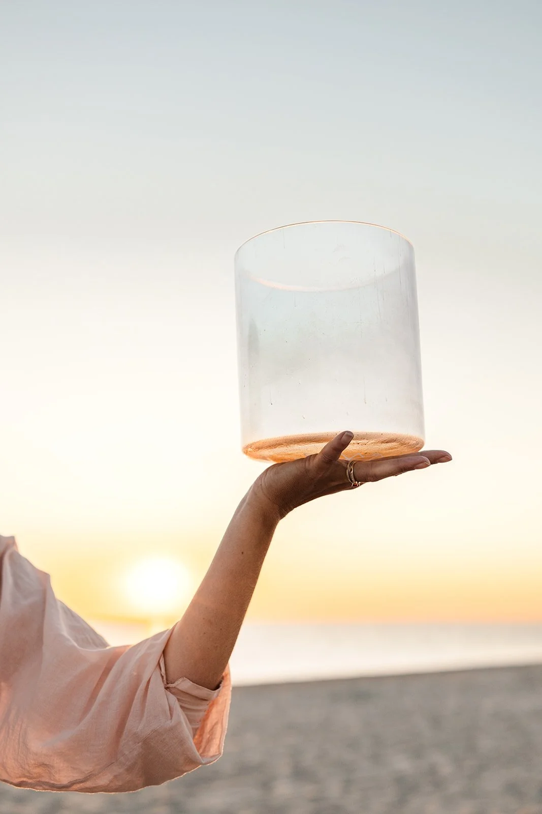 Persoon houdt een glazen cilinder omhoog tijdens zonsondergang op het strand.