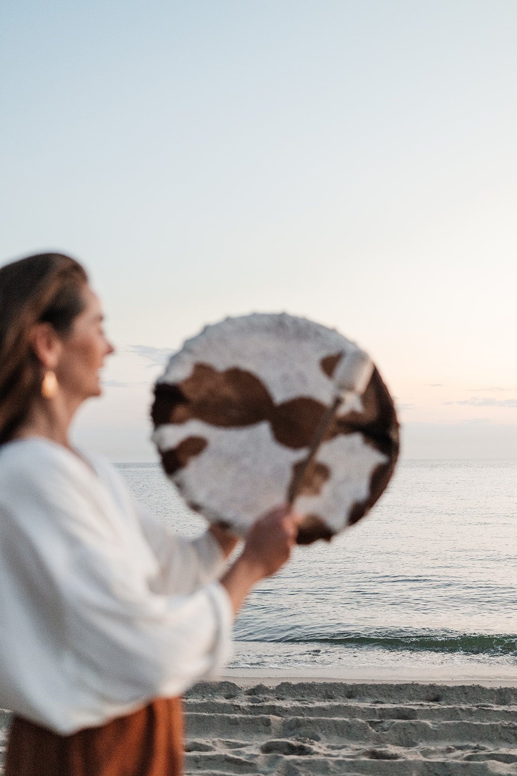Vrouw die een voetbal vasthoudt op het strand bij zonsondergang.