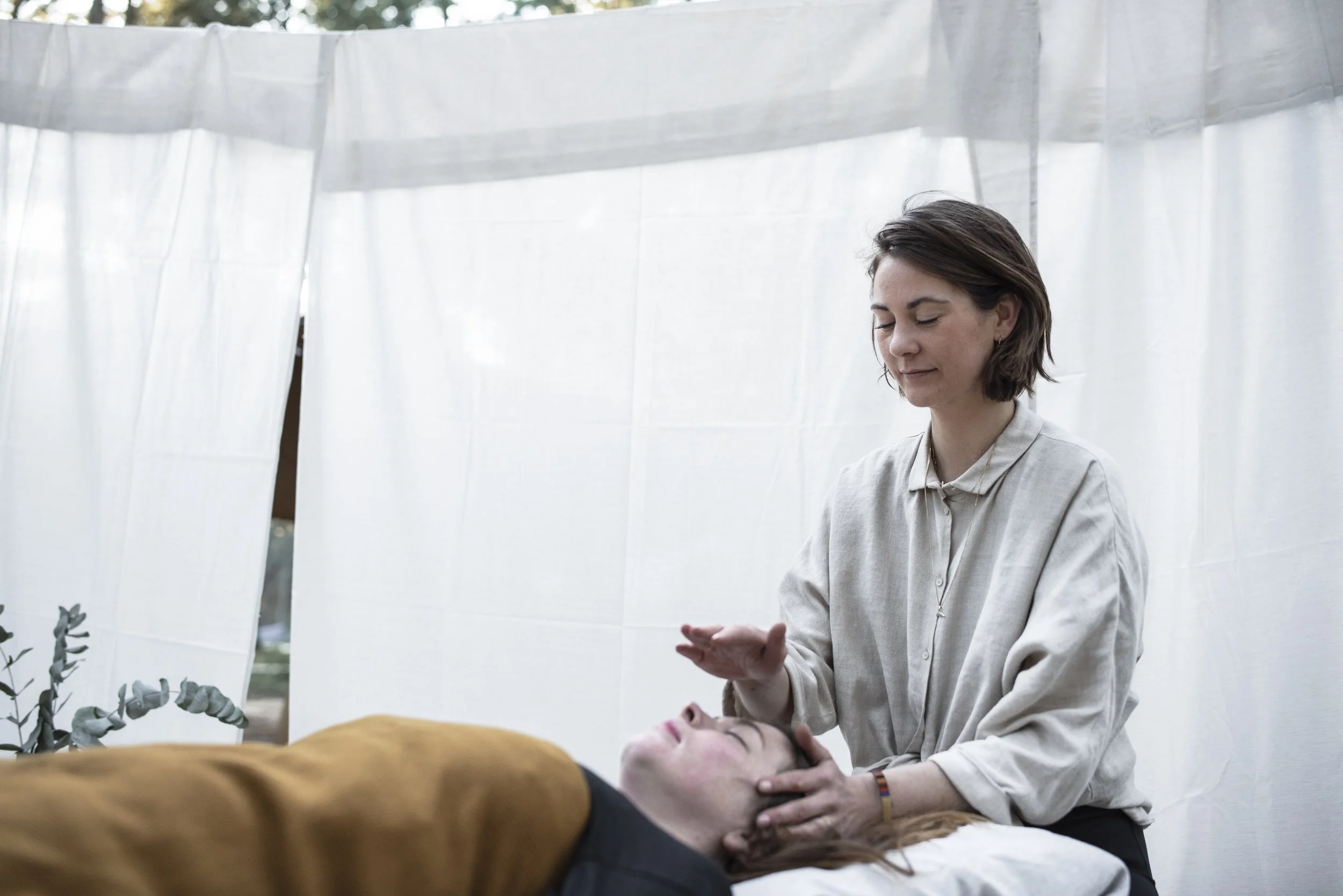 Woman receiving a reiki massage or treatment from another woman in a clinical setting with white curtains, which is an energetic healing service