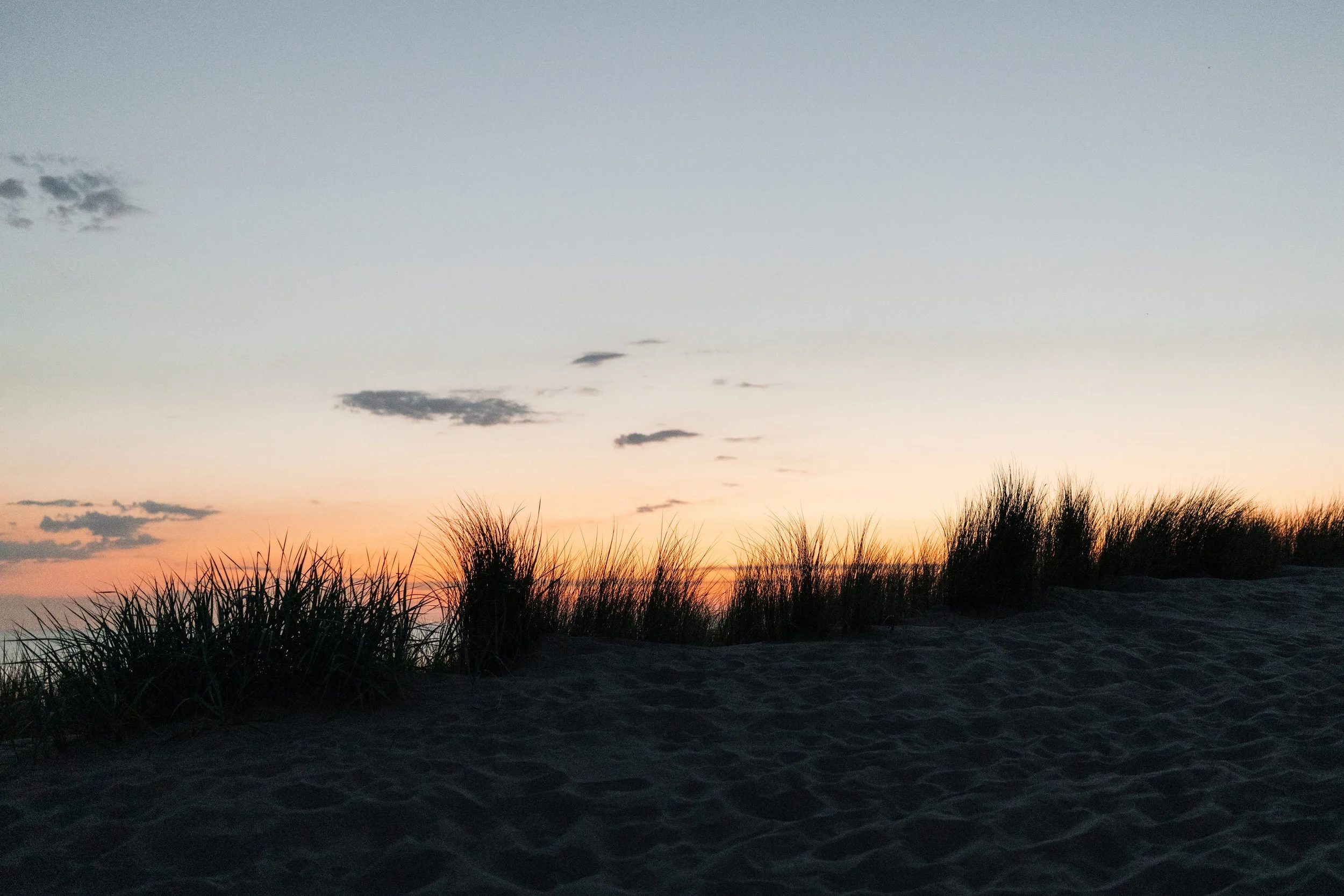 Zonsondergang boven strand met laaghangende duinen en gras.
