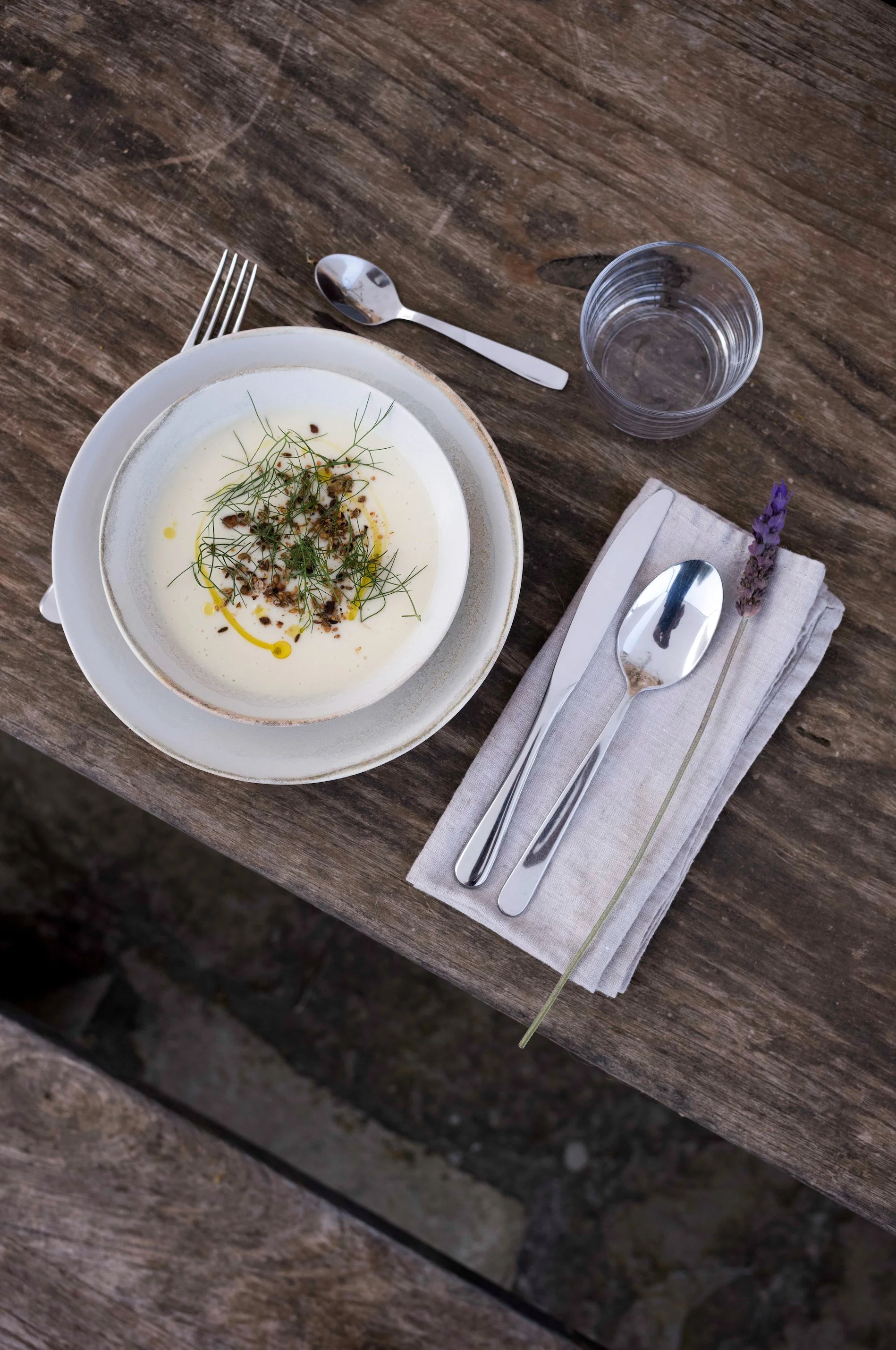 Een bord met een gerecht, een mes, een vork, een lepel, een glas water, een witte servet en een lavendelbloem op een houten tafel. Een heerlijk gerecht tijdens een retraite.