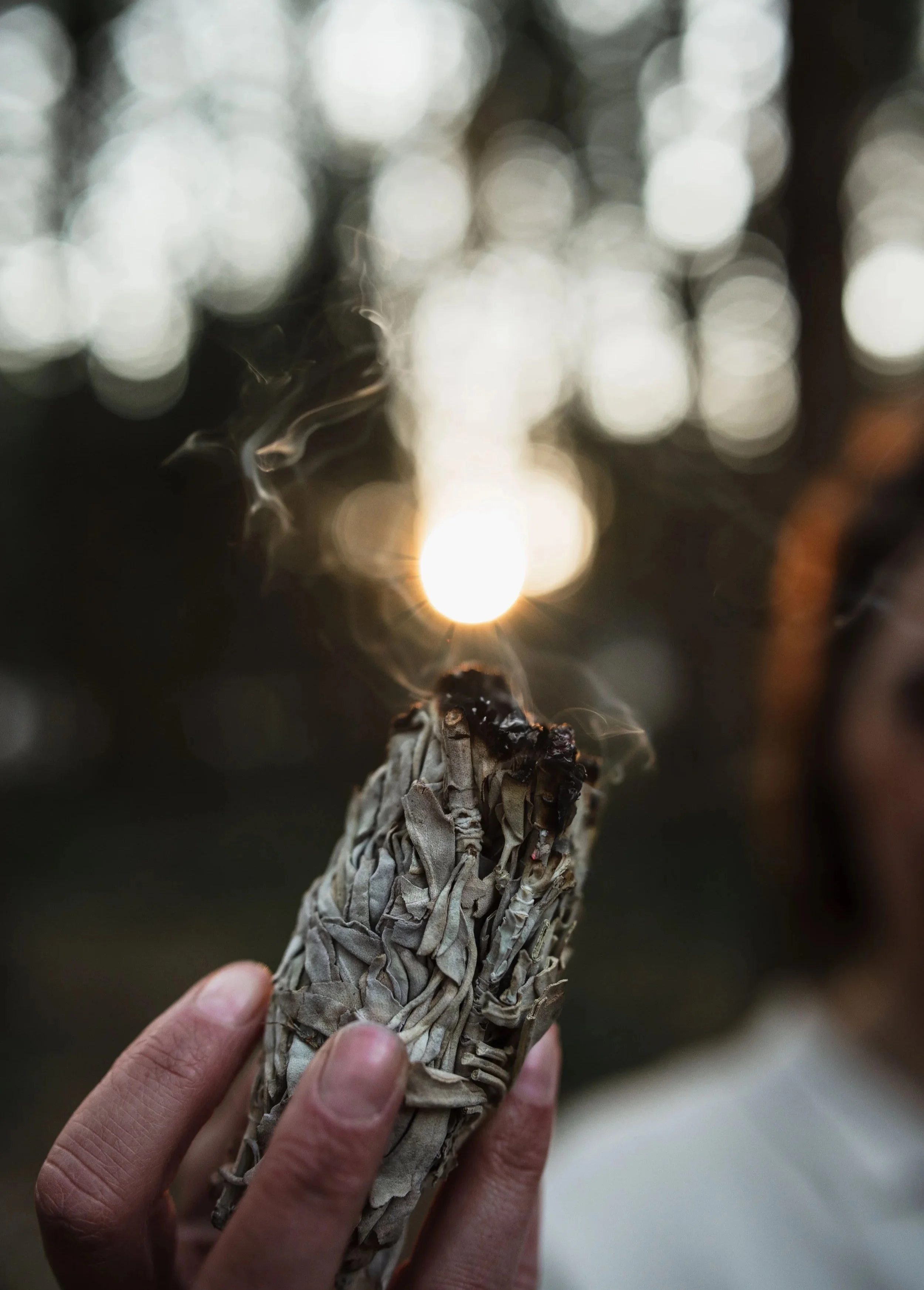 Een hand houdt een opgerolde smeulende smudge stick met witte as.