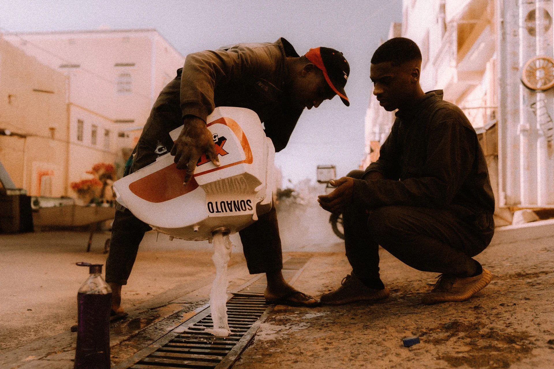 Two men on a street, washing a fuel tank out in a street in Zagora, Morocco.  Shot from the film 100 Kicks in the Desert. Shot from the Brake Magazine film 100 Kicks in the Desert. © Richard Kurowski