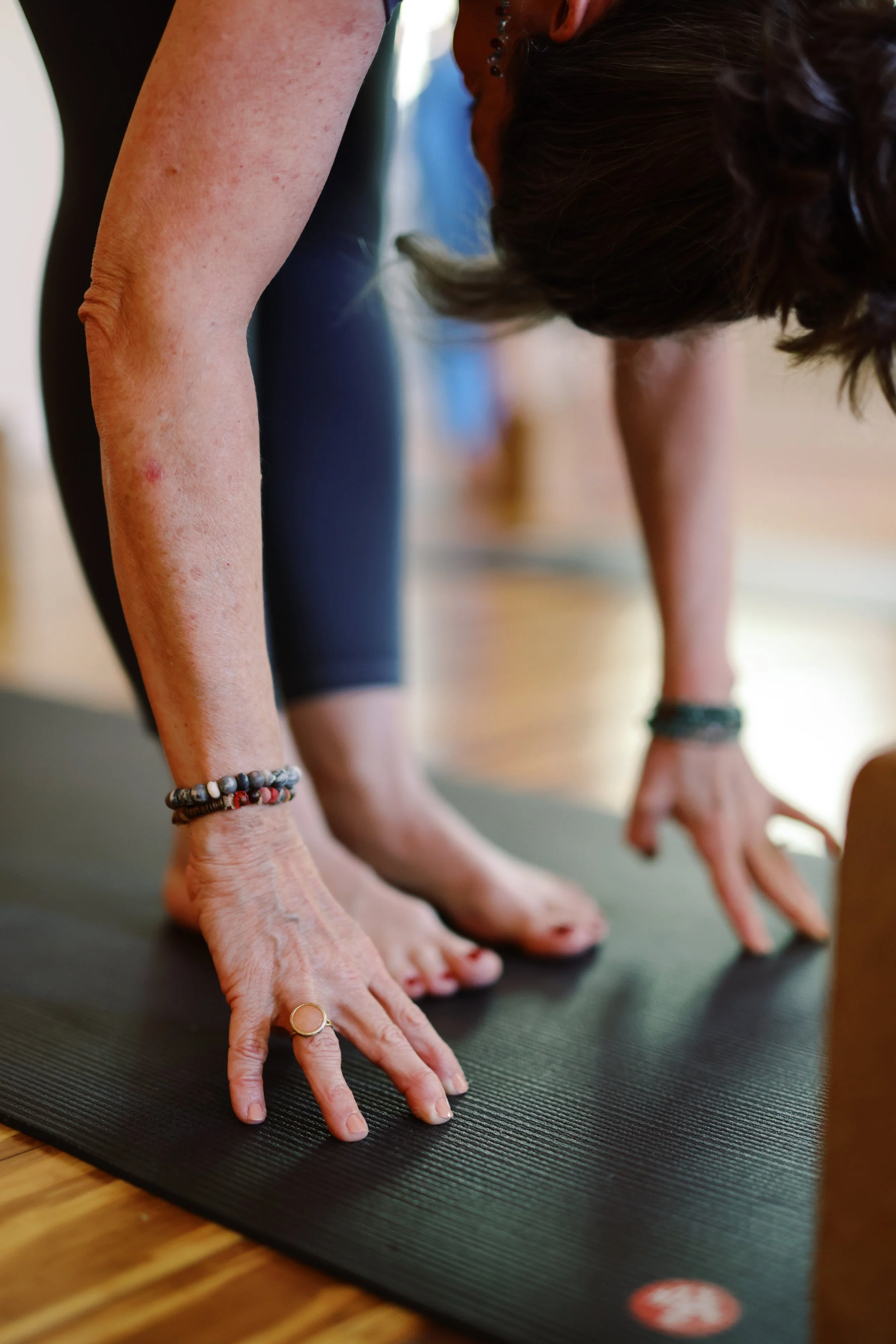 People practicing yoga on a black yoga mat, hands and feet on the mat, in a downward dog pose.