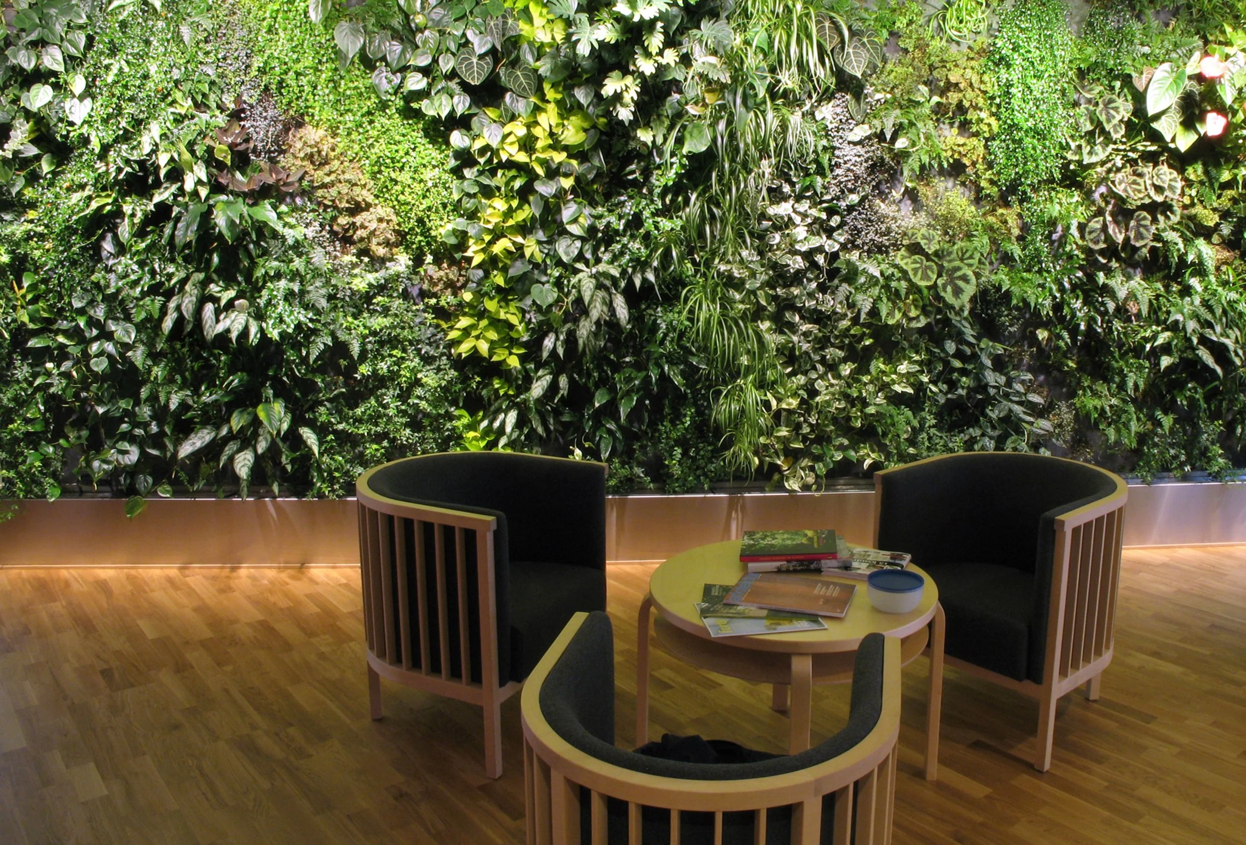 Indoor seating area featuring a large green living wall with various plants, surrounded by chairs.