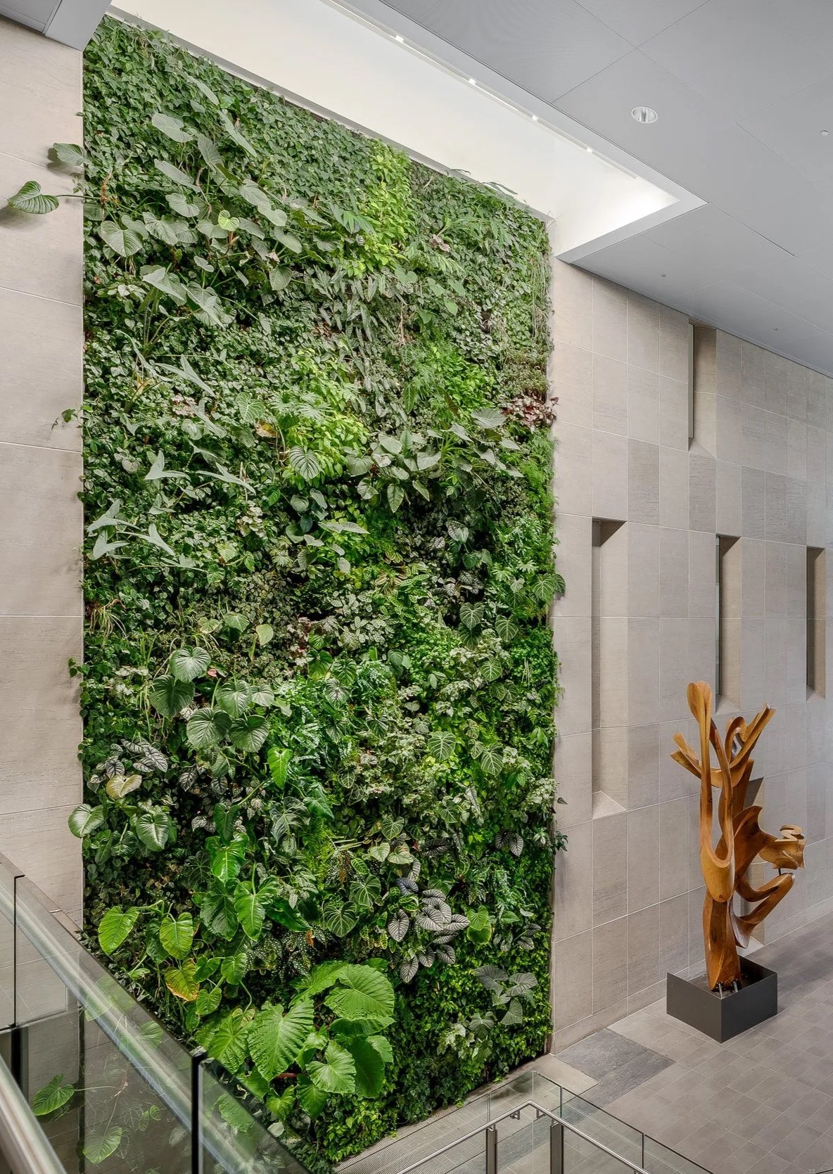 Indoor vertical green wall with various plants and a wooden sculpture nearby.