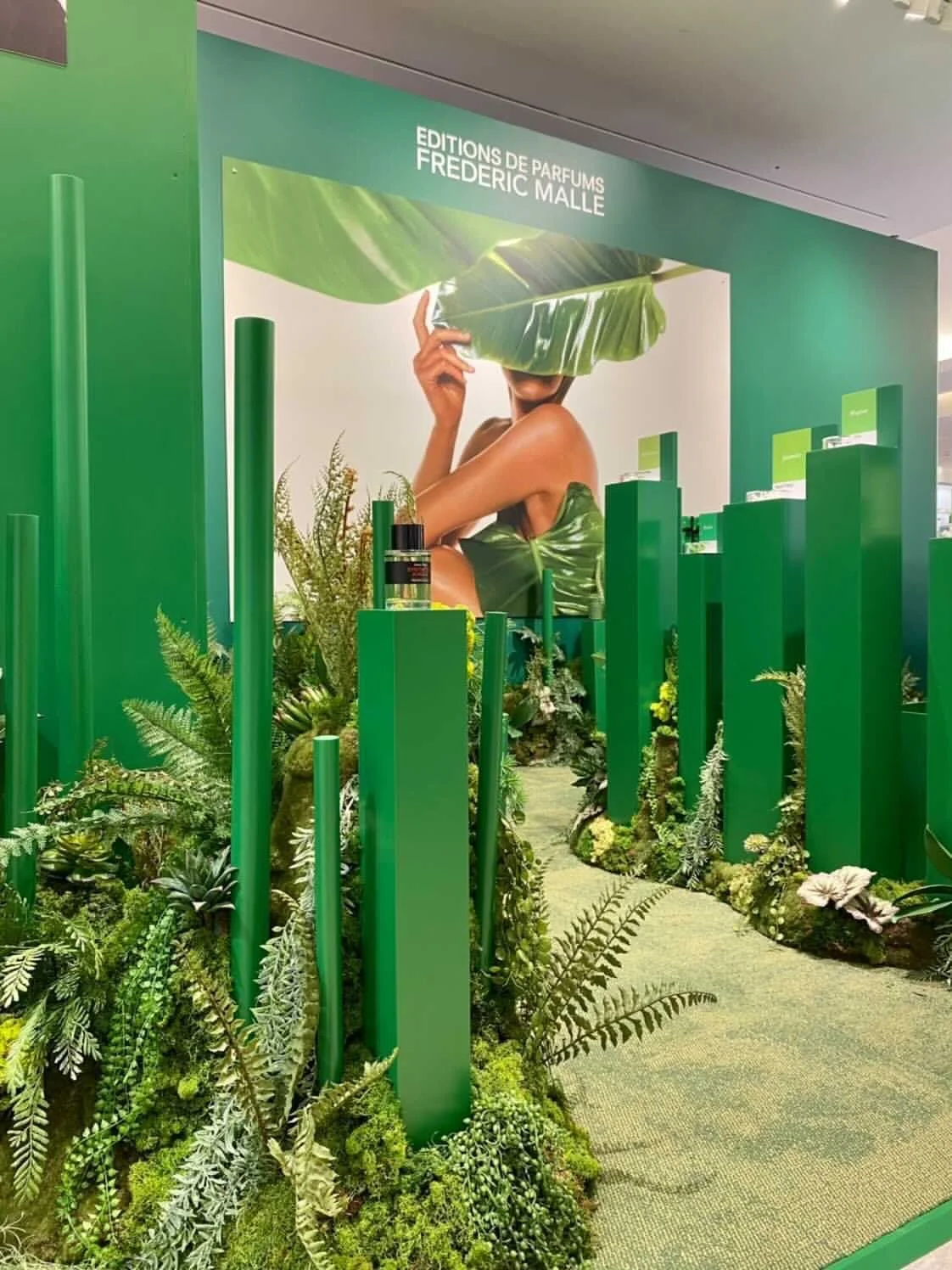 A store display with green vertical pillars and lush moss hills with a jungle inspired design, promoting Frederic Malle 'Synthetic Jungle' perfume.