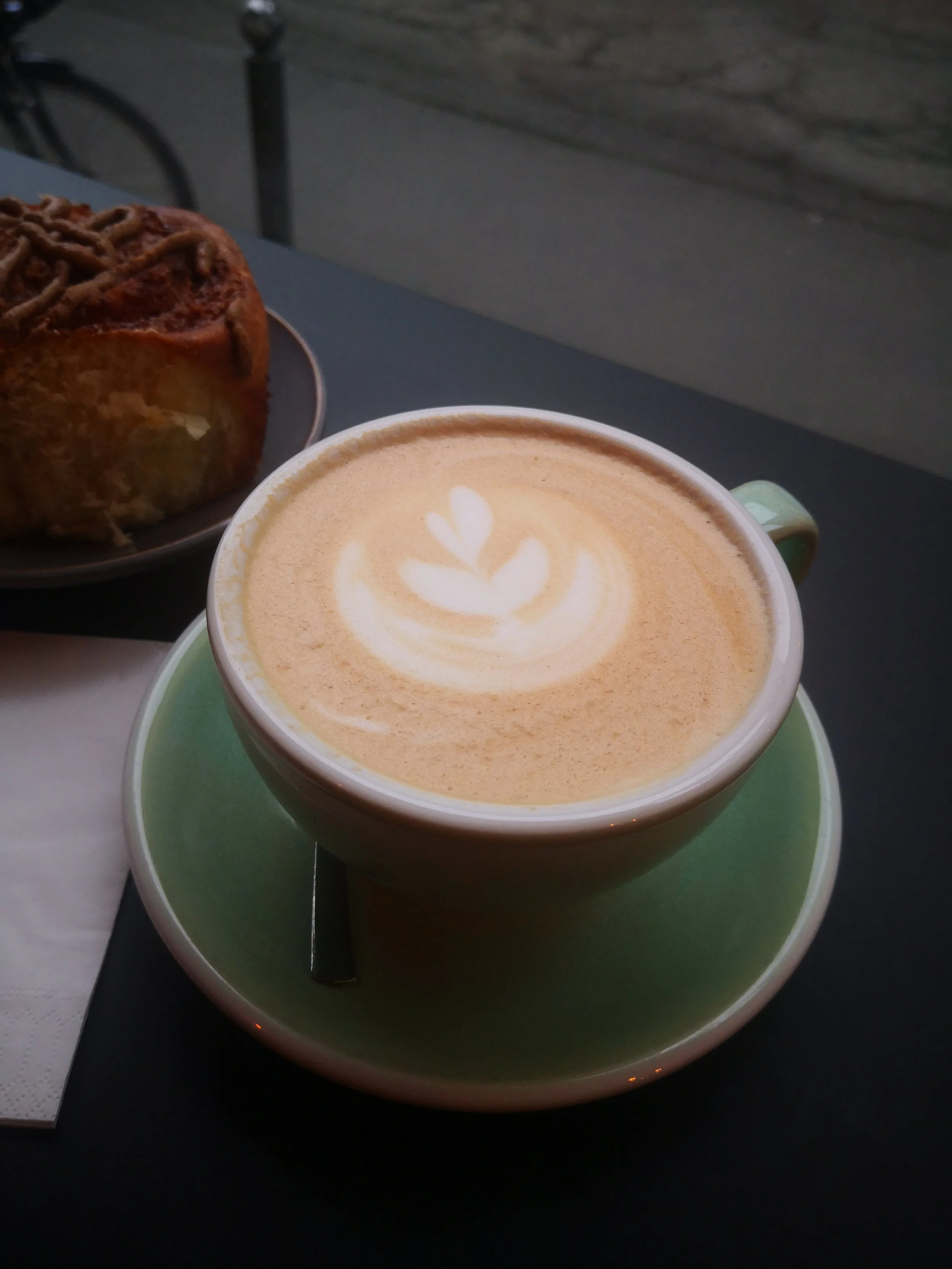Une tasse de café cappuccino avec du lait en forme de cœur, placée sur une soucoupe verte.
