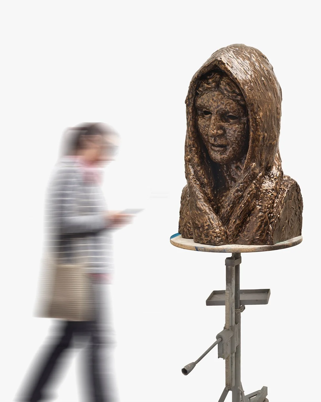 A bronze sculpture of a woman's bust on a stand, with a person blurred out in motion in the background.