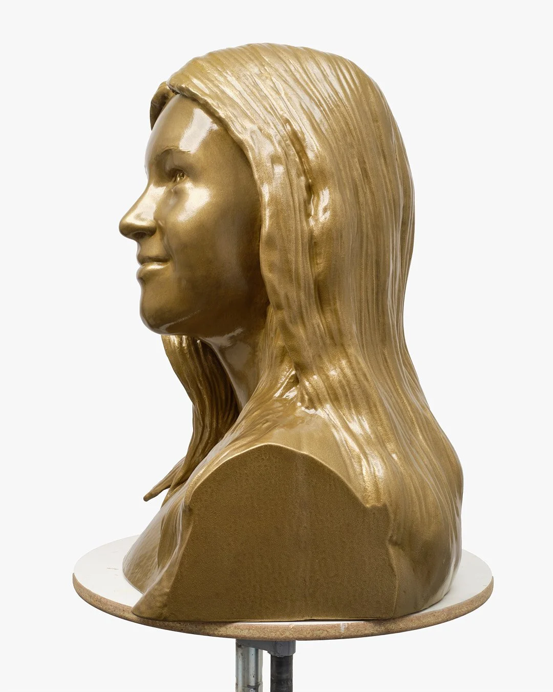 Golden bust sculpture of a woman's profile with long hair, mounted on a round base.