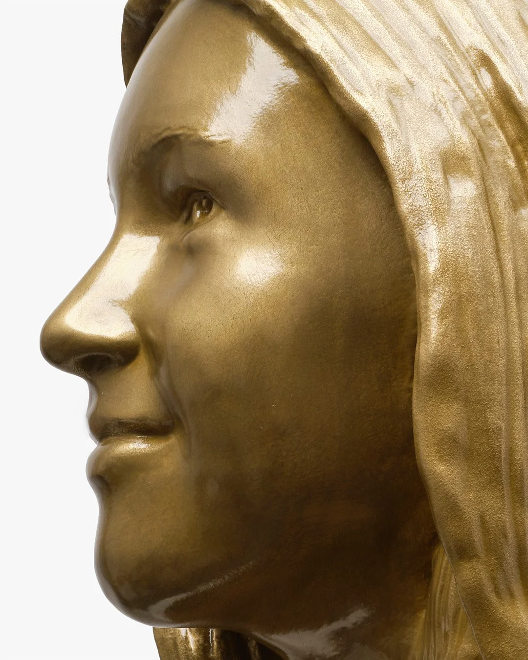 Close-up of a gold-colored sculpture of a person's face in profile, showing detailed features and flowing hair.