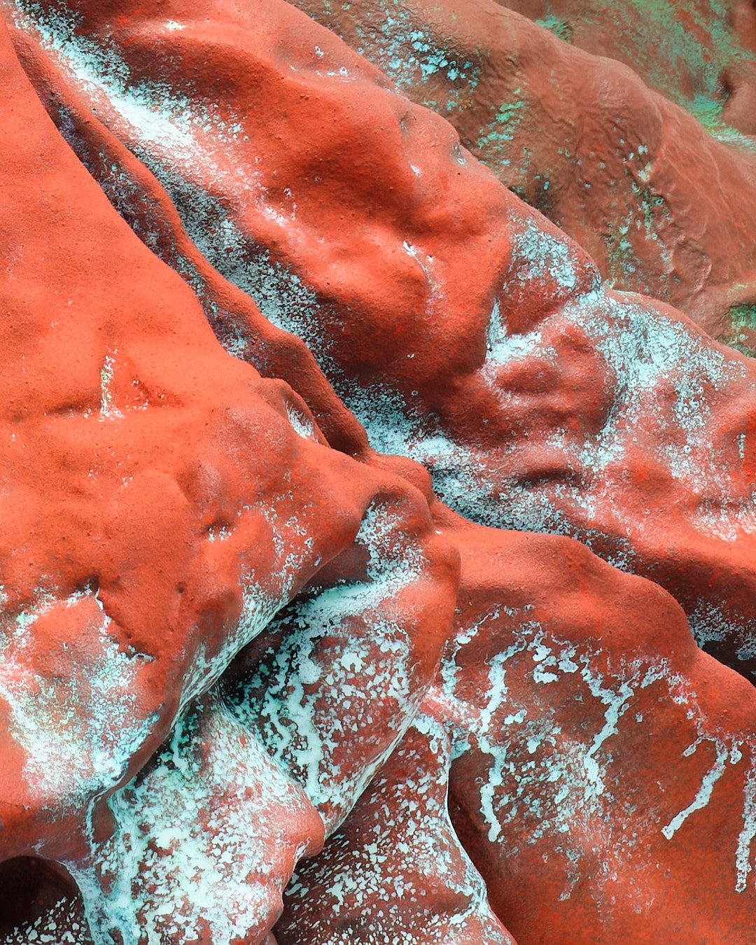 Close-up of red clay with patches of white and blue lichen or mineral deposits.