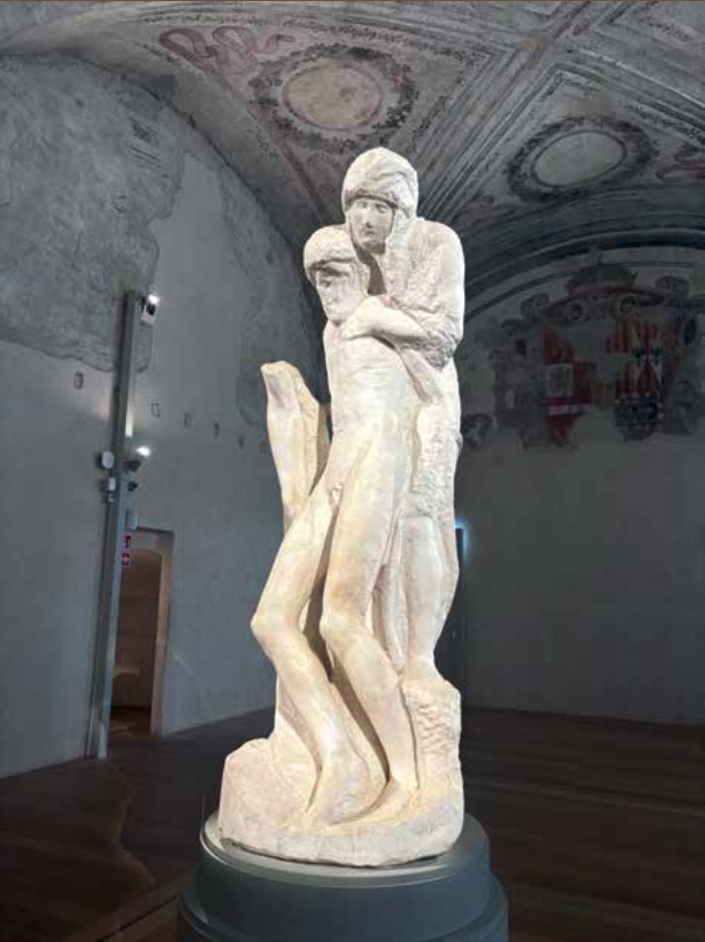 A white stone sculpture of a couple embracing, located inside a room with a decorated ceiling.