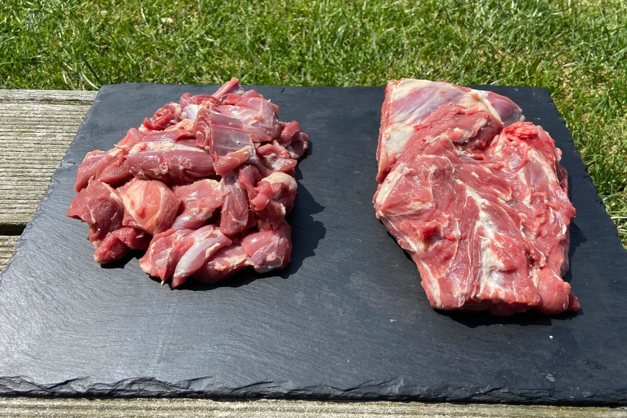 Chopped raw meat on a black slate board outdoors, with a grassy background.
