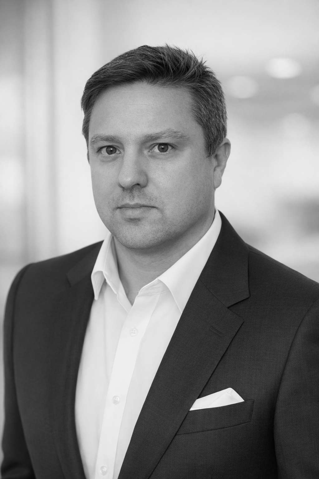 A young man in a suit sitting indoors with artwork on the wall behind him.