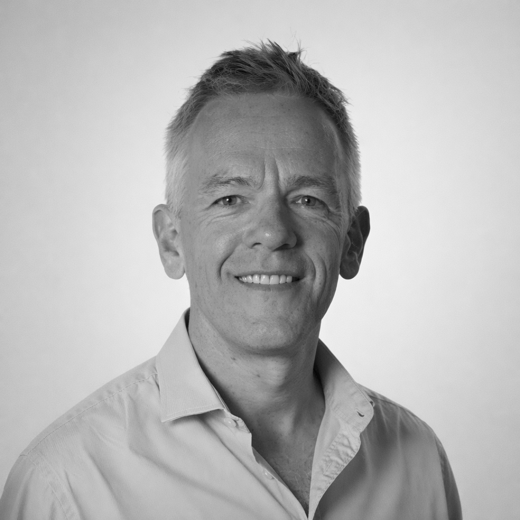 A black and white portrait of a man smiling outdoors.