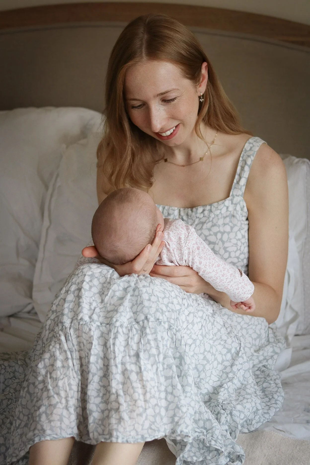 A woman with red hair smiling while holding a baby in a bedroom.