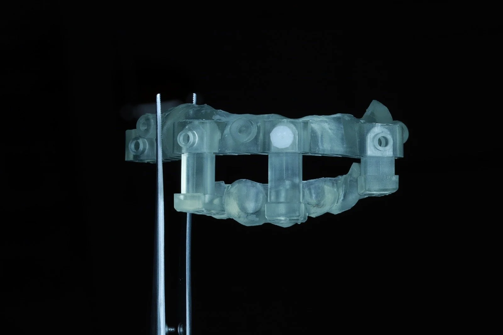 A translucent, 3D-printed wrist brace or support mounted on two metal rods against a black background.