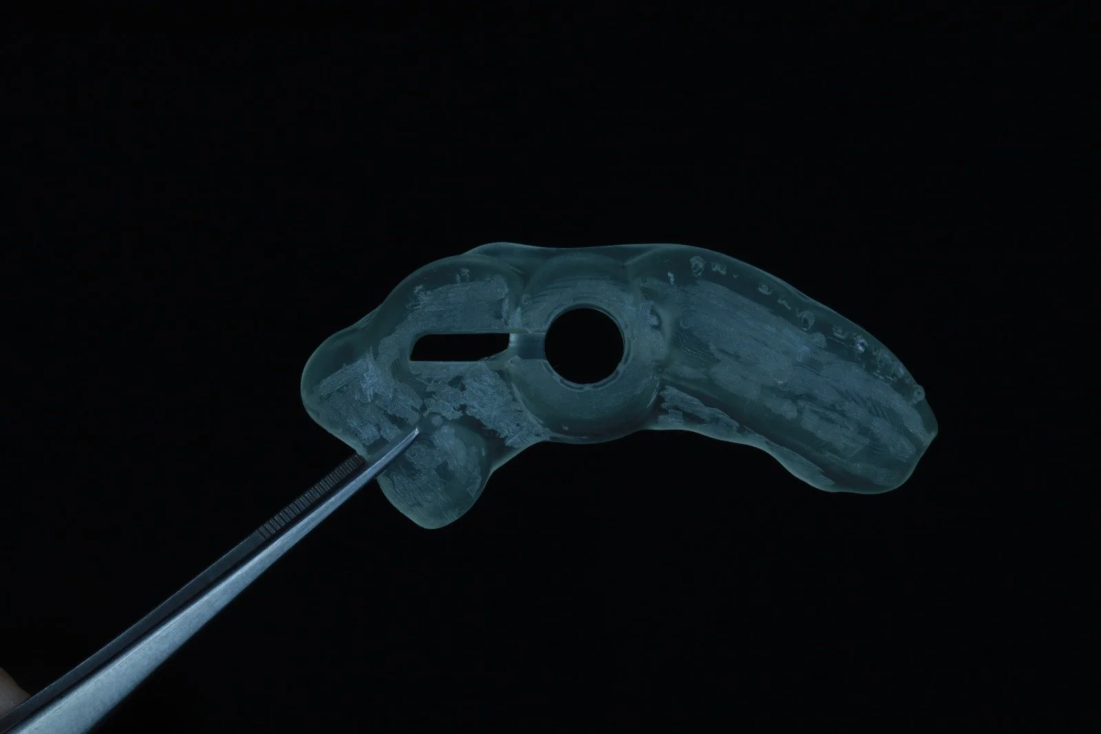 A clear dental surgical guide being prepared with a precision tool against a black background.