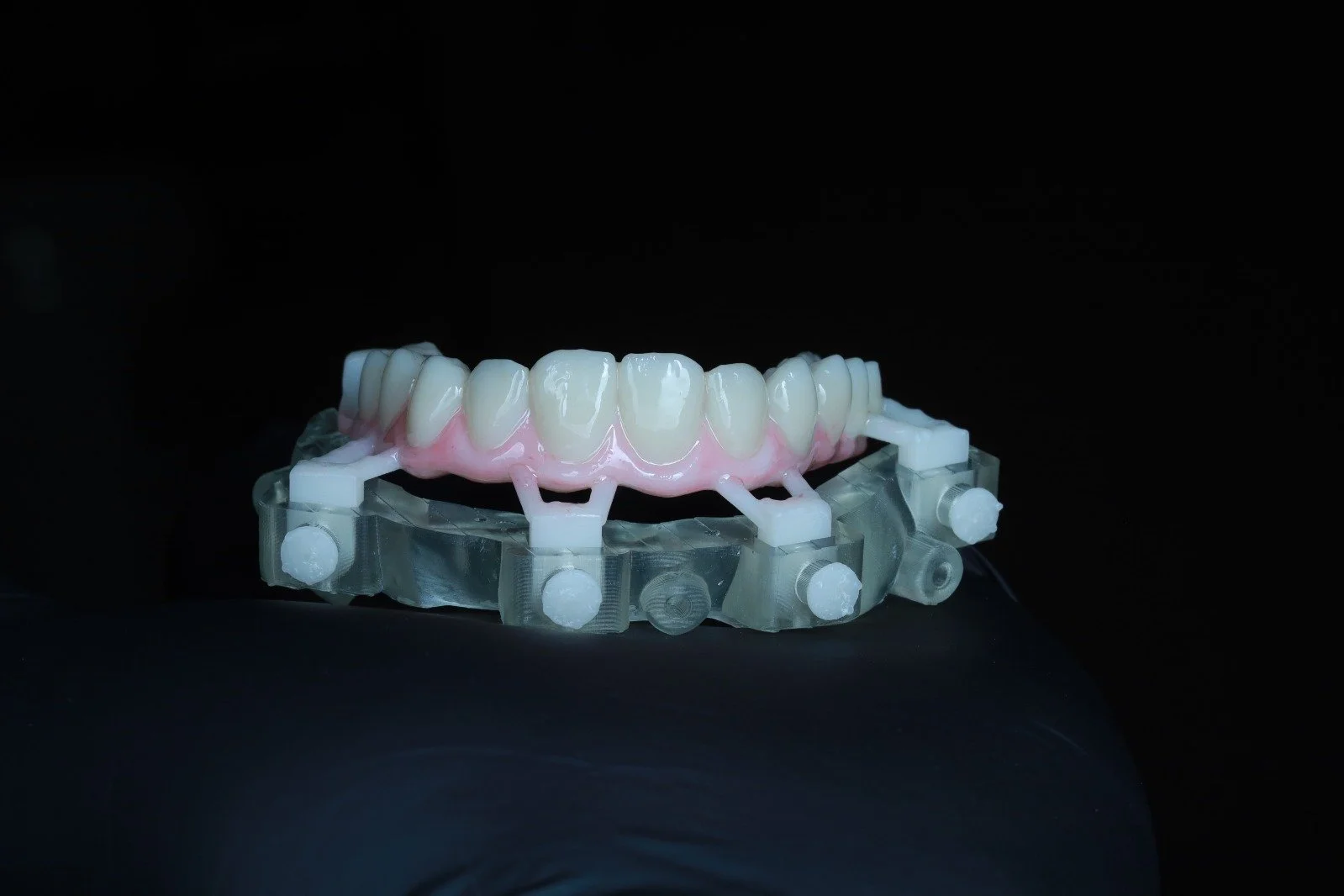 Dental prosthetic with simulated teeth mounted on a clear orthodontic device against a black background.