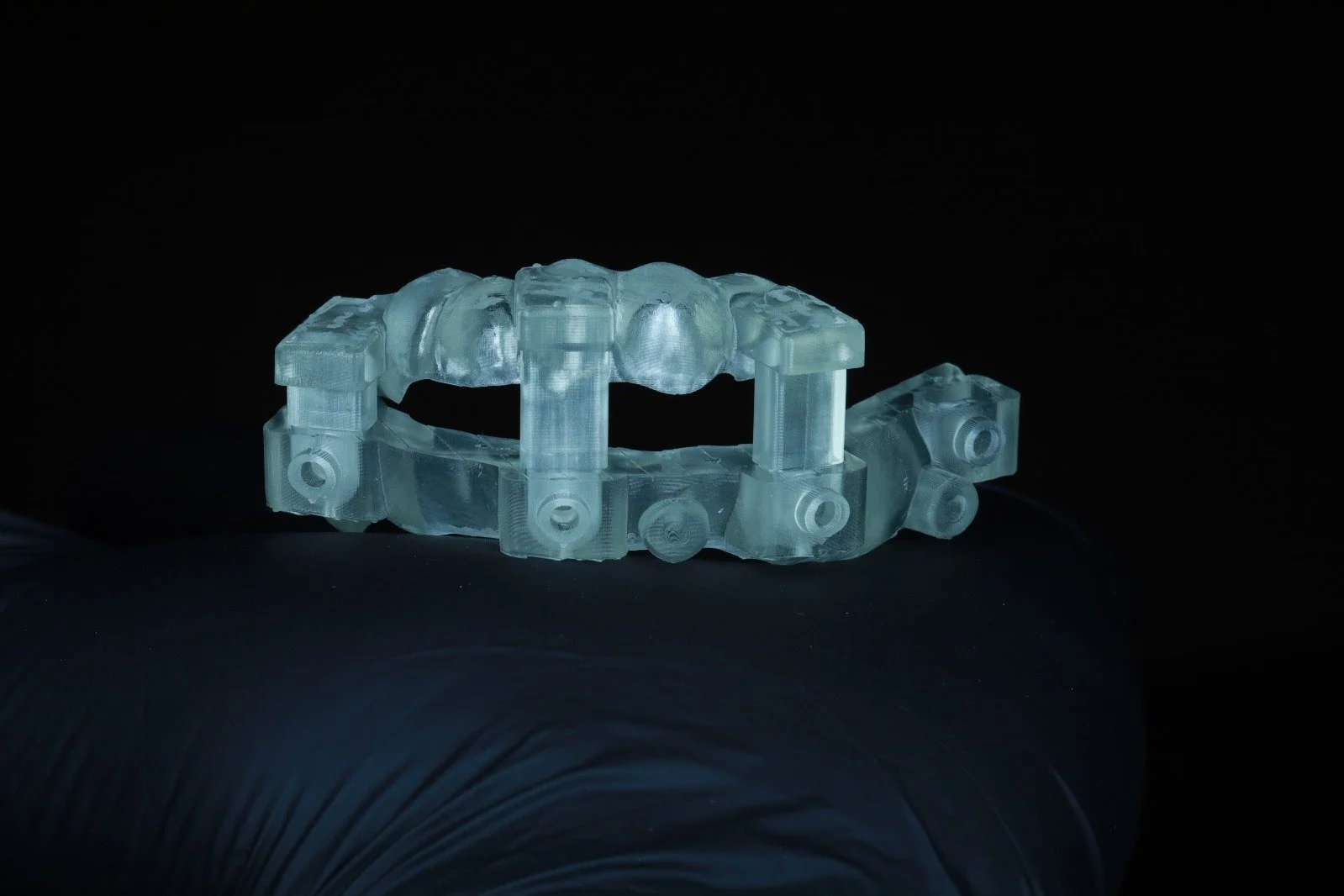 A transparent dental aligner with multiple tooth impressions, resting on a dark surface.