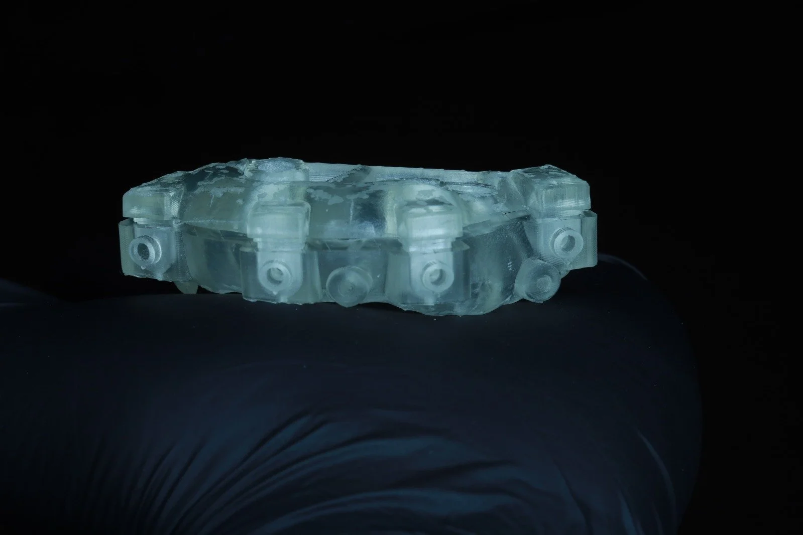 A clear, translucent dental implant abutment held on a person's finger against a black background.