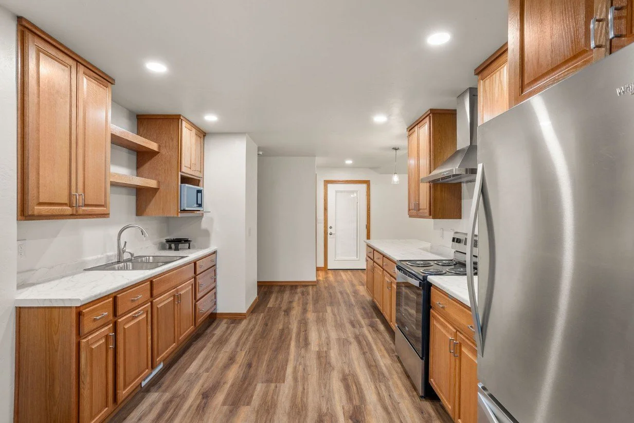 Kitchen with wooden cabinets, white countertops, stainless steel appliances, and wood flooring.