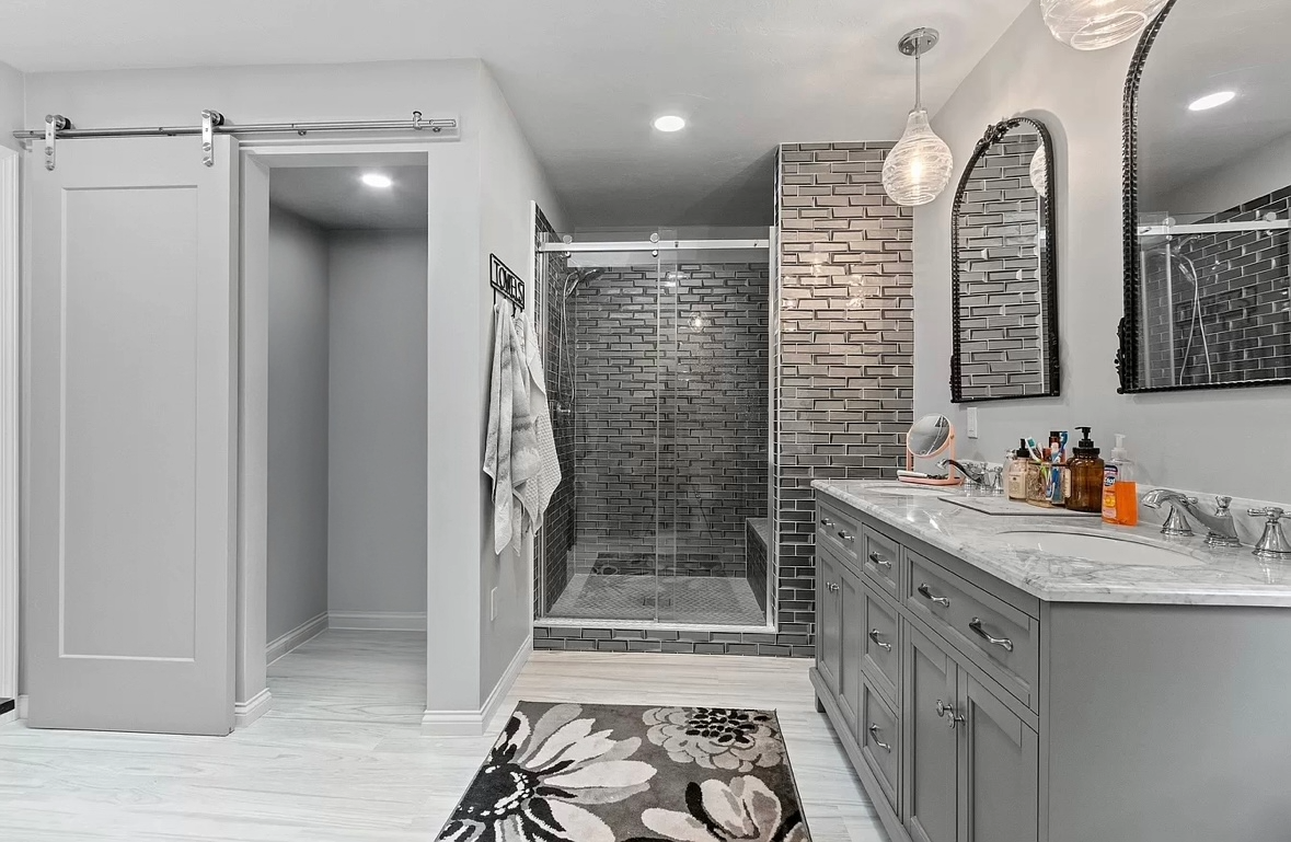 Modern bathroom with a walk-in shower with glass doors, white and gray cabinetry, a marble countertop, and decorative mirrors on the wall.