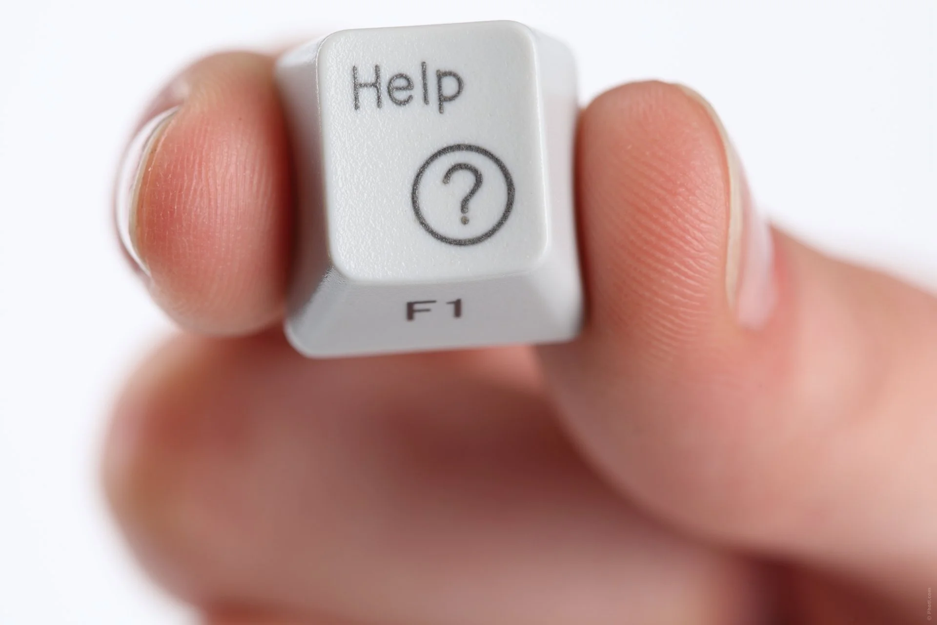 Close-up of a person's hand holding a white computer keyboard key labeled 'Help' with a question mark icon, and 'F1' key below.