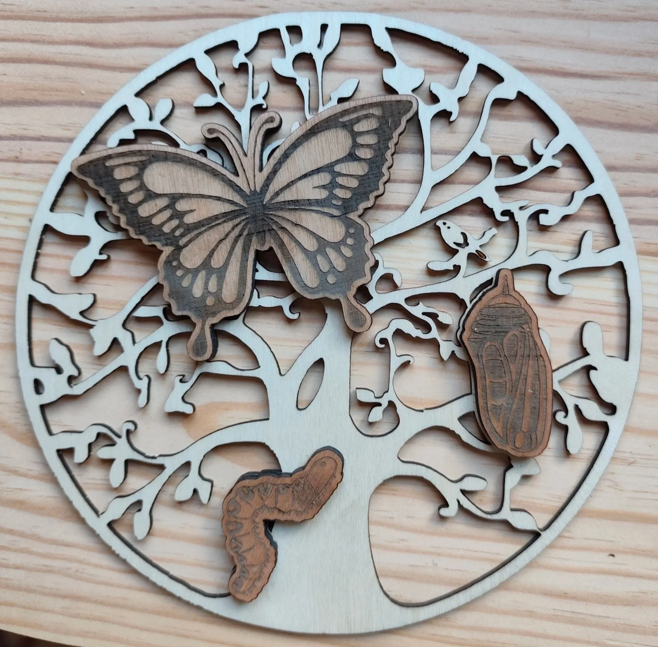 Décoration en bois représentant un arbre, une papillon, une coccinelle, une chenille, symbolisant l'évolution du papillon