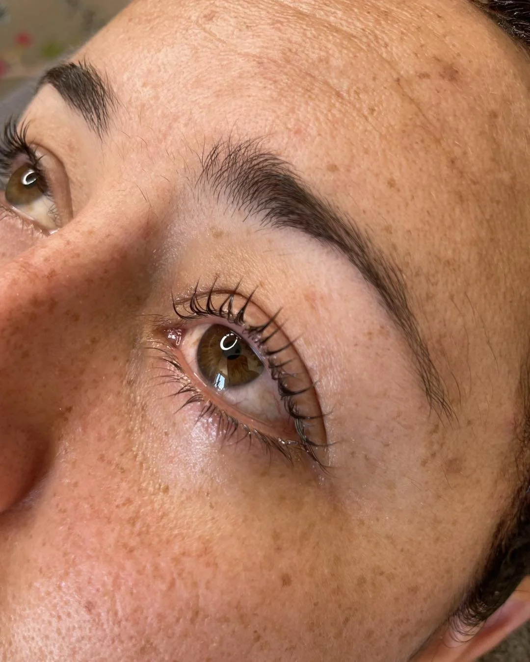 Close-up of a person's face, focusing on brown eyes, thick eyebrows, and freckles on their skin.