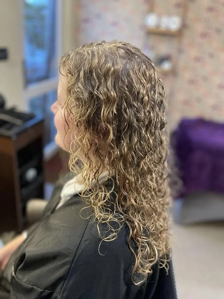 A woman with wet, curly hair sitting in a salon chair.