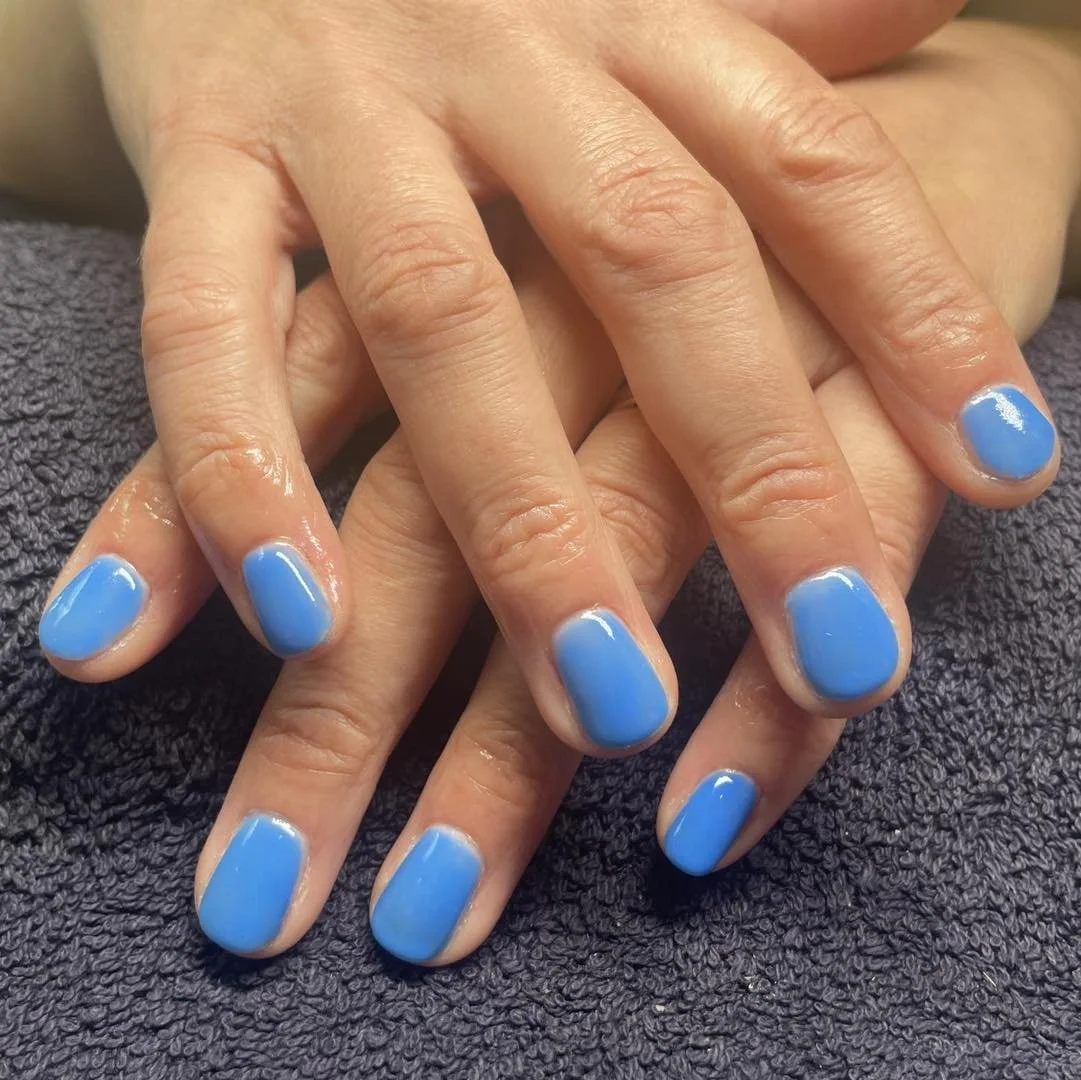 Hands with blue painted fingernails resting on a dark towel.