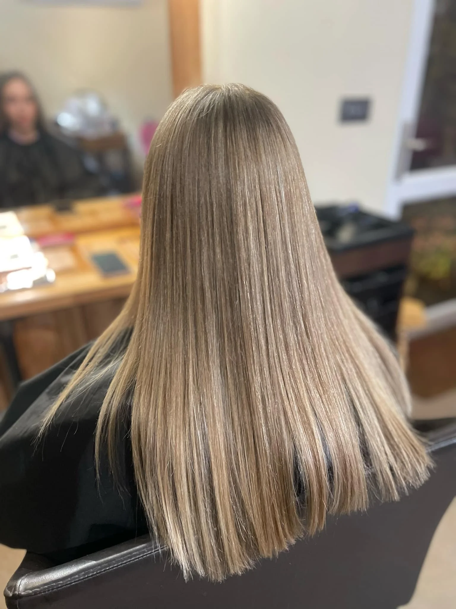 Blonde hair with darker roots, straight and smooth, on a person sitting in a salon chair.