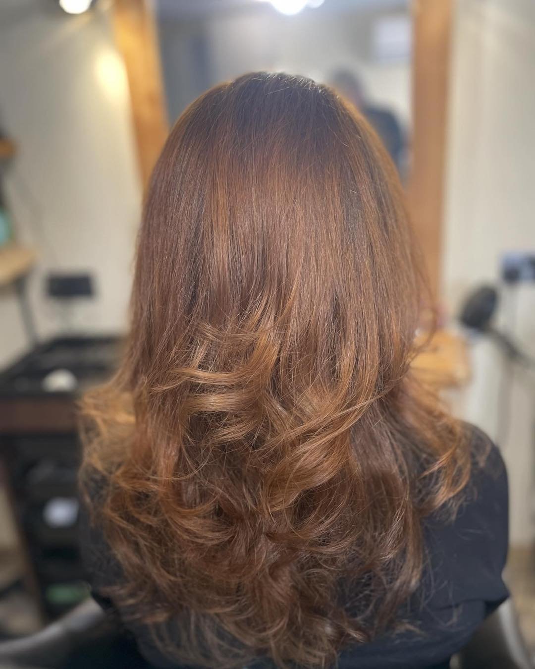 Back view of a woman with shoulder-length, wavy, reddish-brown hair.