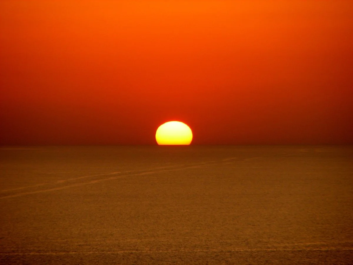 Solo, sun resting on the sea horizon, suspended in an instant of light.