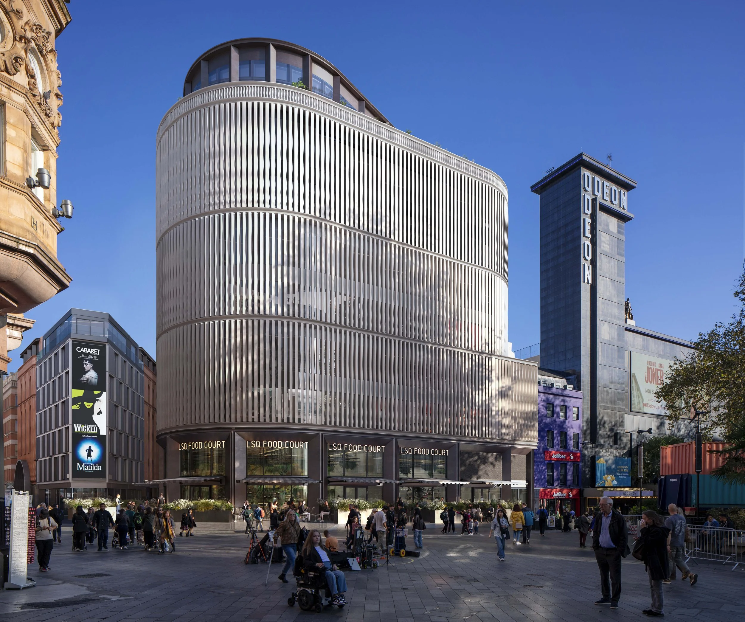 Proposed LSX Development. Modern building with curved, metallic facade and glass windows, labeled LSX Food Court, in London Leicester Square with pedestrians, some using wheelchairs, around it.